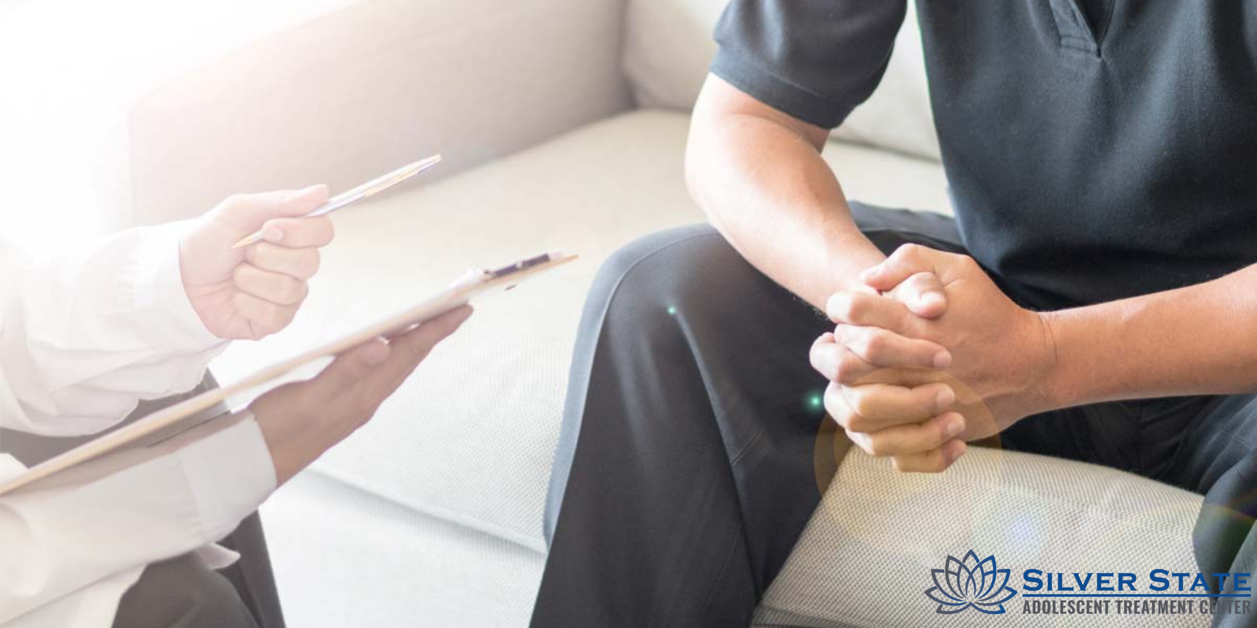 A teen sits on a couch with hands clasped while another holds a clipboard and pen, suggesting an adolescent mental health counseling session. The Silver State Adolescent Treatment Center logo is visible in the bottom right corner.